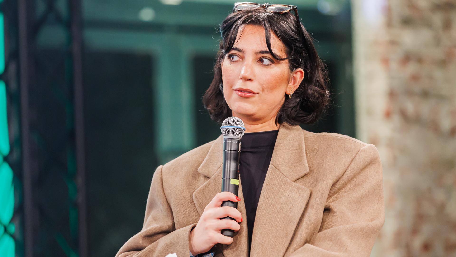 Aya Jaff hält ein Mikrofon in der Hand und nimmt an einem Podiumsgespräch teil.