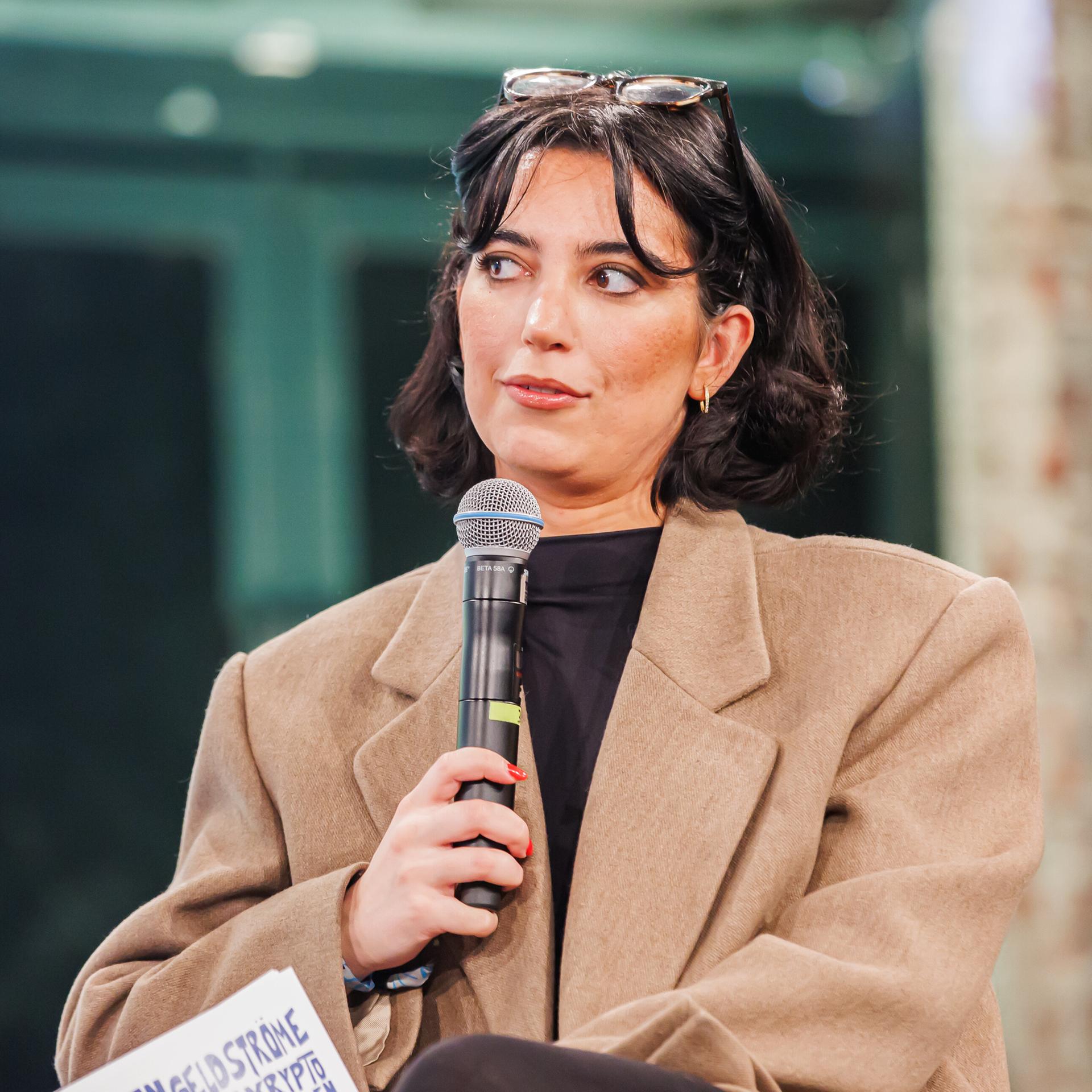 Aya Jaff hält ein Mikrofon in der Hand und nimmt an einem Podiumsgespräch teil.