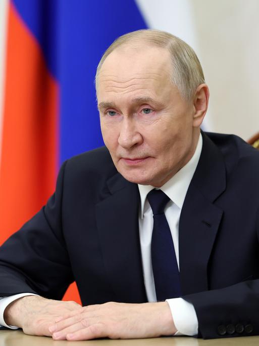 Der russische Präsident Wladimir Putin sitzt an einem Tisch und spricht in eine Kamera.