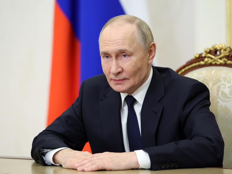 Der russische Präsident Wladimir Putin sitzt an einem Tisch und spricht in eine Kamera.