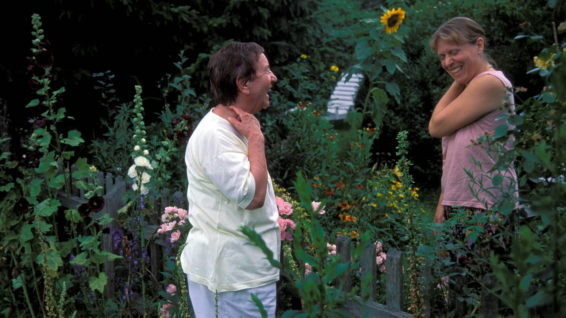 Zwei Frauen stehen beim Gespräch am Gartenzaun zwischen ihren Gärten und lachen. Zwei Frauen stehen beim Gespräch am Gartenzaun zwischen ihren Gärten und lachen.