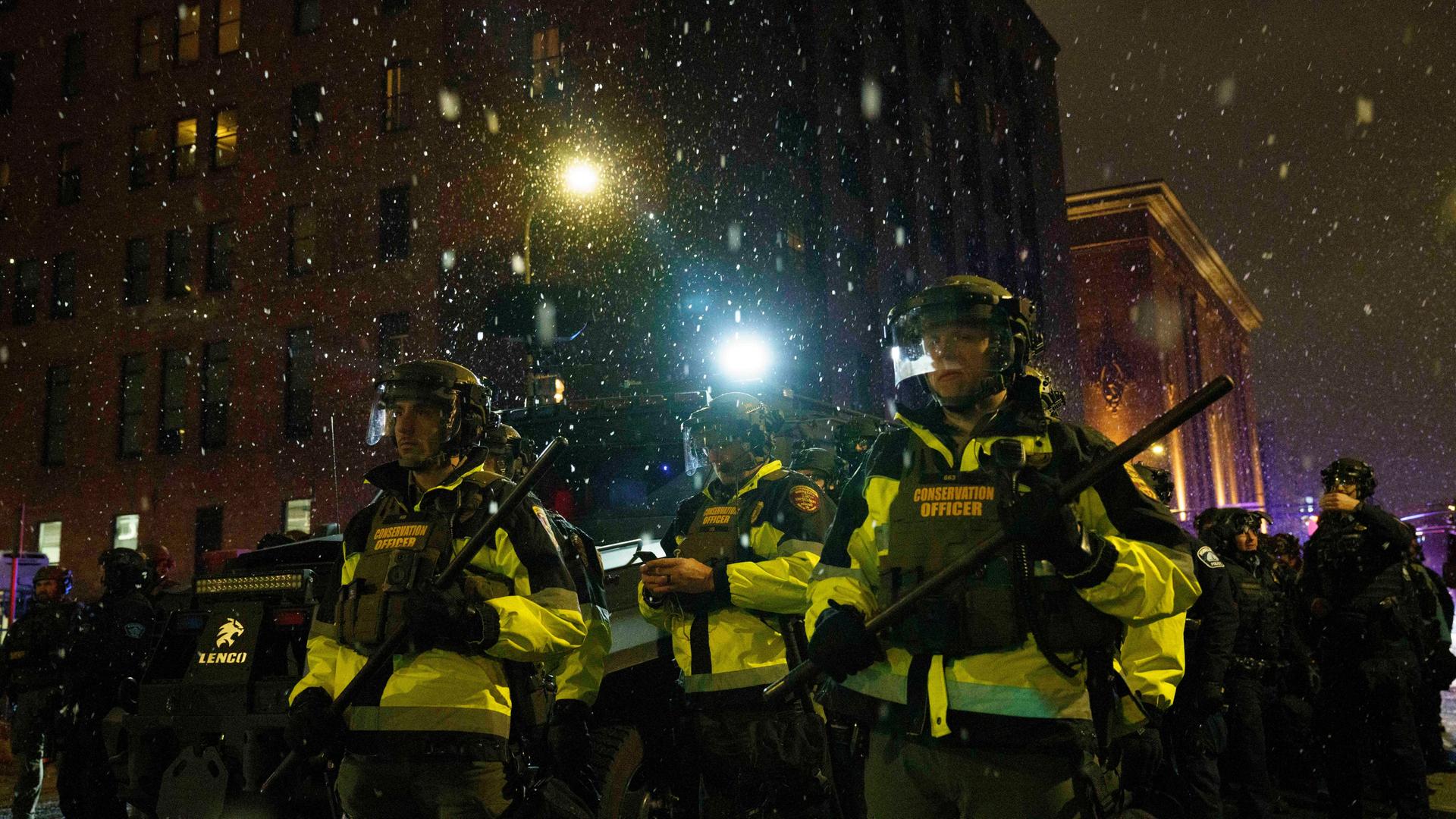 Polizeibeamte stehen auf einer Staße in Minneapolis. Sie tragen Schlagstöcke. Es ist dunkel und schneit. Polizeibeamte stehen auf einer Staße in Minneapolis. Sie tragen Schlagstöcke. Es ist dunkel und schneit.