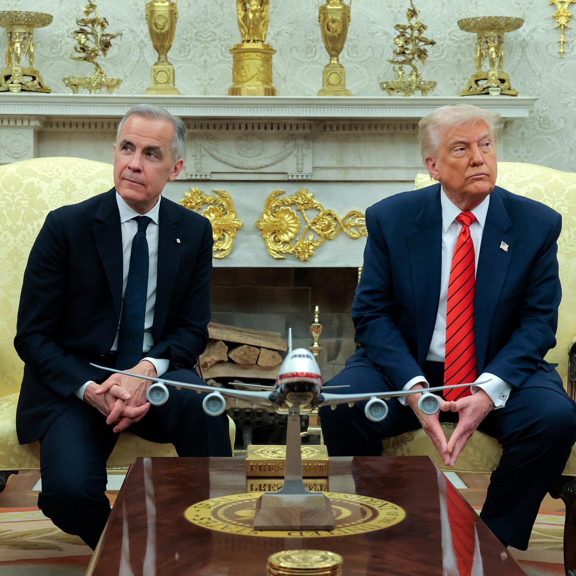 Der kanadische Premierminister Carney sitzt neben US-Präsident Trump. Beide schauen ernst und jeweils in eine andere Richtung.  