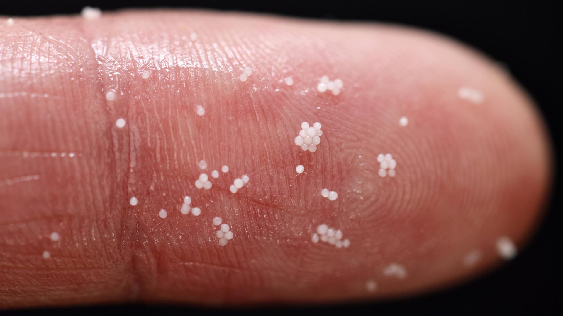Weiße Mikroplastik-Partikel an einem Finger