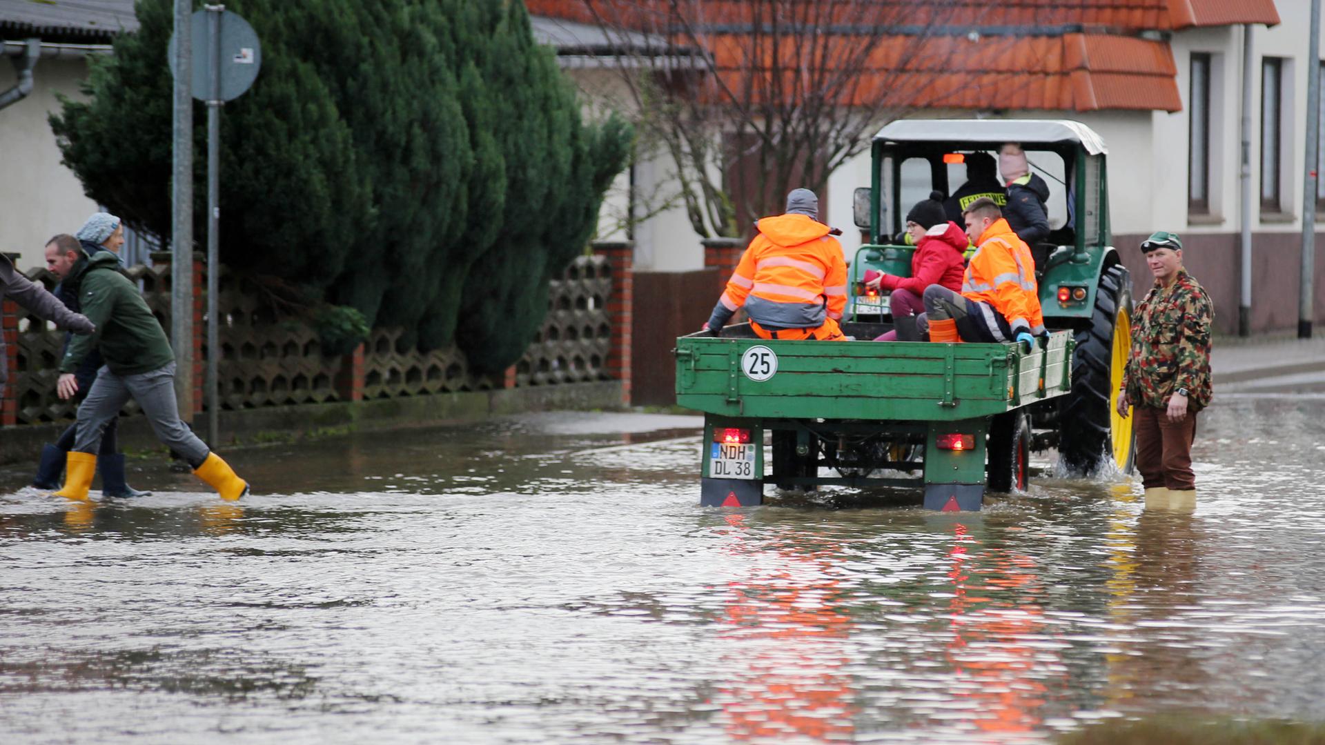 Ein Traktor mit Anhänger, auf dem Menschen sitzen, fährt durch eine überflutete Straße