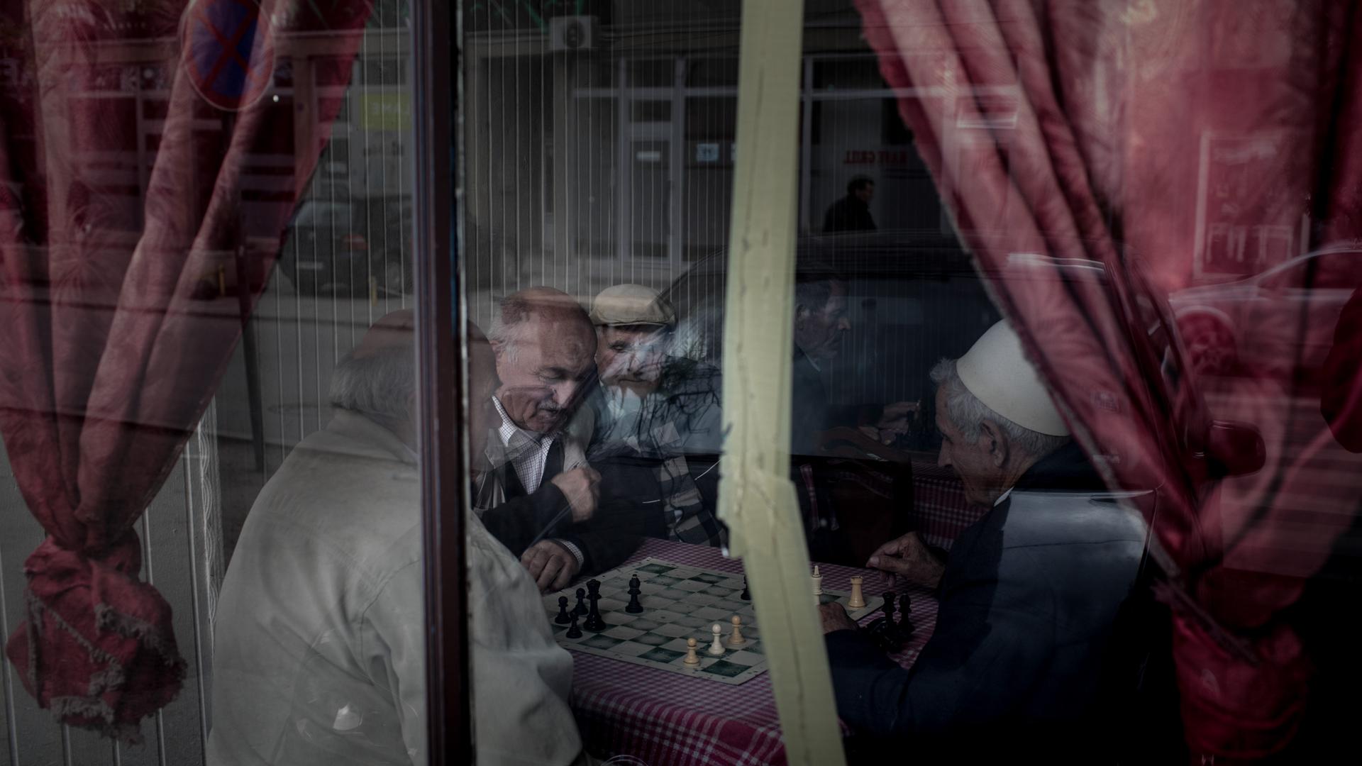 Blick durch die Scheibe eines Cafés, in dem Männer für ein Schachspiel beieinander sitzen.