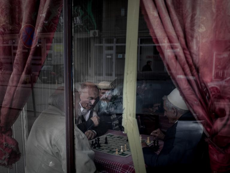 Blick durch die Scheibe eines Cafés, in dem Männer für ein Schachspiel beieinander sitzen.