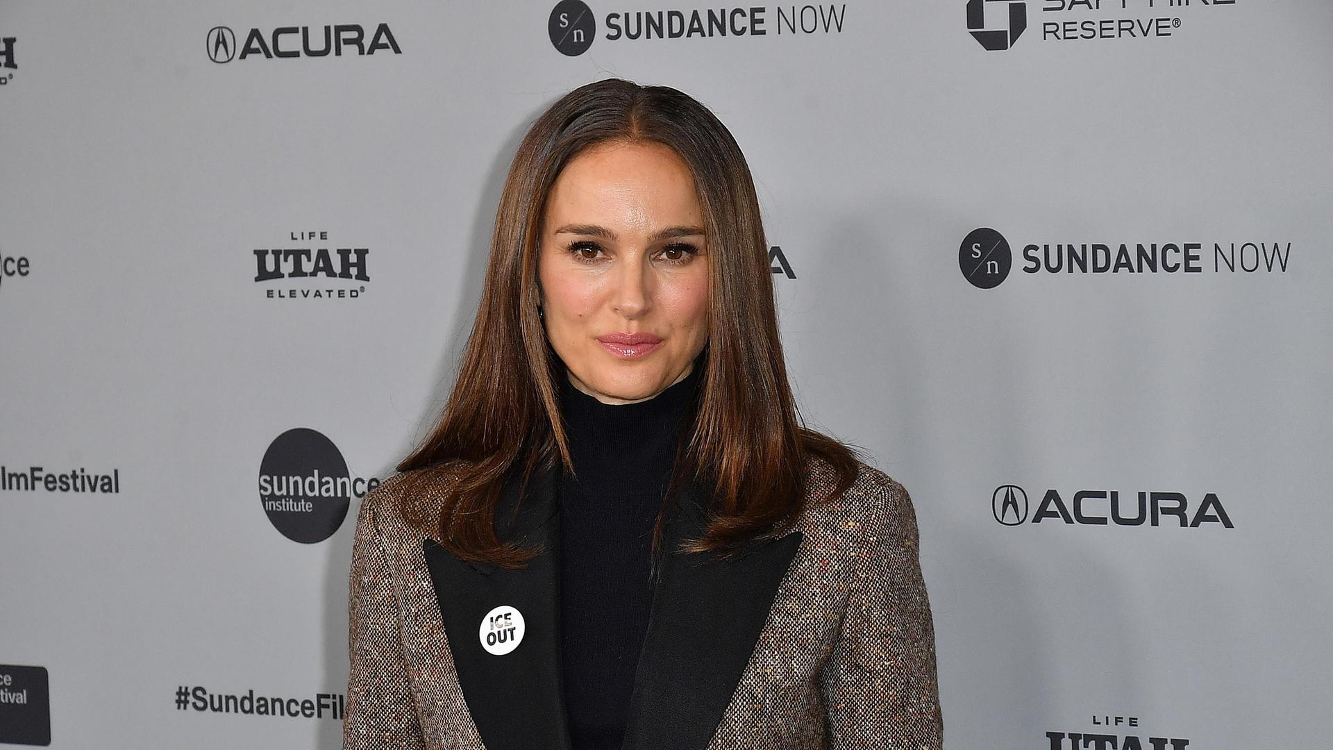 Natalie Portman steht vor einer Werbewand. Sie trägt einen Button, auf dem Ice out steht