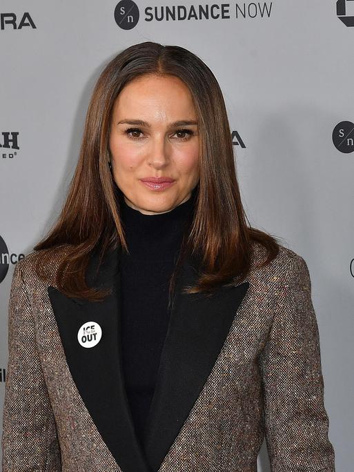 Natalie Portman steht vor einer Werbewand. Sie trägt einen Button, auf dem Ice out steht