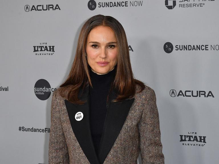 Natalie Portman steht vor einer Werbewand. Sie trägt einen Button, auf dem Ice out steht