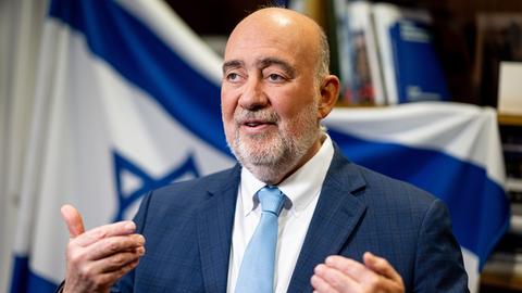 Ron Prosor, Botschafter Israels in Deutschland, steht vor einer israelischen Flagge und gestikuliert mit den Händen.
