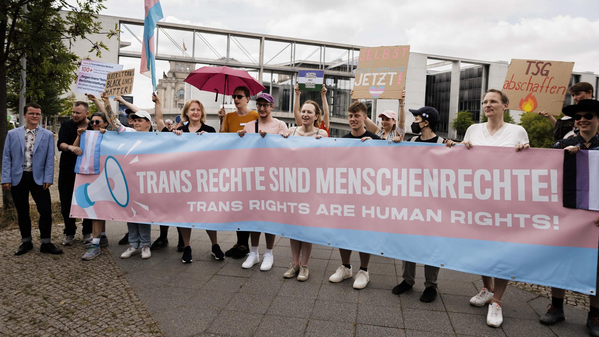 Lisa Paus hält gemeinsam mit Demonstranten ein Transparent in blau und rosa, auf dem steht: "Trans Rechte sind Menschenrechte." 