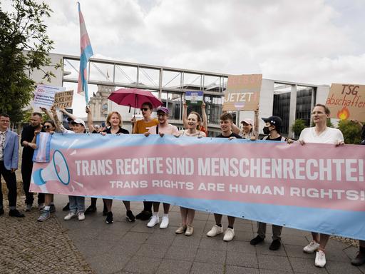 Lisa Paus hält gemeinsam mit Demonstranten ein Transparent in blau und rosa, auf dem steht: "Trans Rechte sind Menschenrechte." 