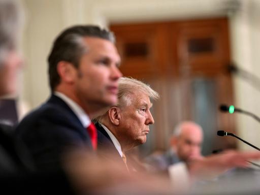 Zwei Männer sitzen an einem Tisch. Vor ihnen Mikrofone. Der jüngere Mann im Vordergrund ist unscharf. Beide blicken zum rechten Bildrand. Zwei Männer sitzen an einem Tisch. Vor ihnen Mikrofone. Der jüngere Mann im Vordergrund ist unscharf. Beide blicken zum rechten Bildrand.