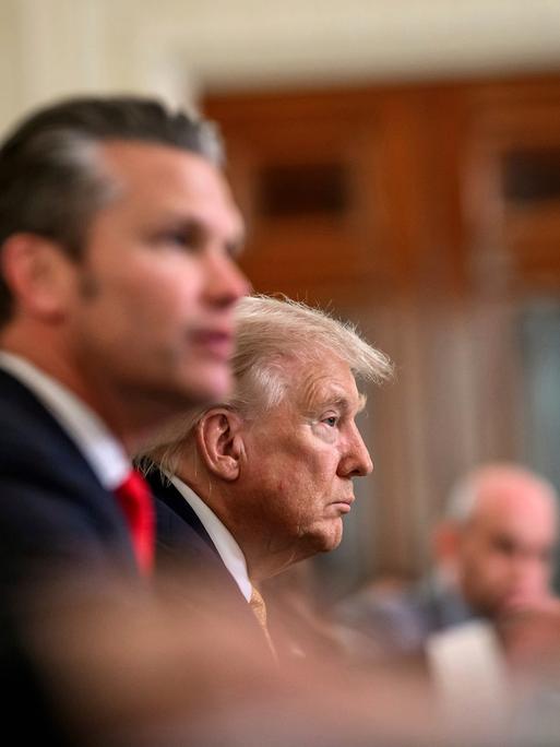 Zwei Männer sitzen an einem Tisch. Vor ihnen Mikrofone. Der jüngere Mann im Vordergrund ist unscharf. Beide blicken zum rechten Bildrand. Zwei Männer sitzen an einem Tisch. Vor ihnen Mikrofone. Der jüngere Mann im Vordergrund ist unscharf. Beide blicken zum rechten Bildrand.