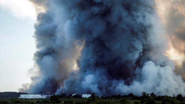 Das Bild zeigt eine große Rauch-Wolke. Die Rauch-Wolke steigt in den Himmel. Unten im Bild ist eine Lager-Halle zu sehen.