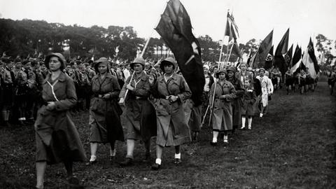 Historisches schwarz-weiß Foto zeigt eine Parade der evangelischen Kirchenorganisationen am 25. Juni 1933. Zu sehen sind auch Fahnen mit dem nationalsozialistischen Hakenkreuz.