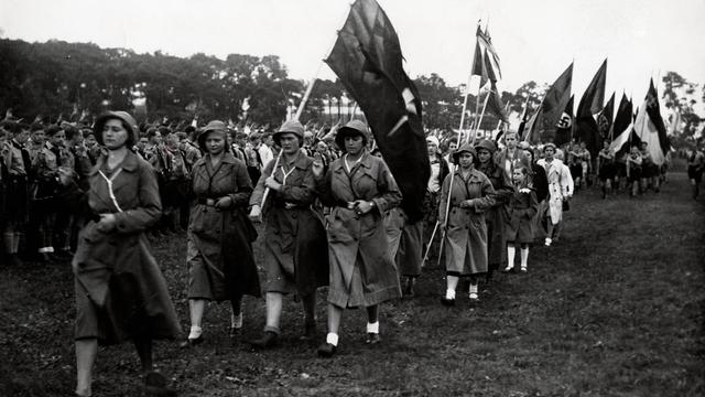 Historisches schwarz-weiß Foto zeigt eine Parade der evangelischen Kirchenorganisationen am 25. Juni 1933. Zu sehen sind auch Fahnen mit dem nationalsozialistischen Hakenkreuz.