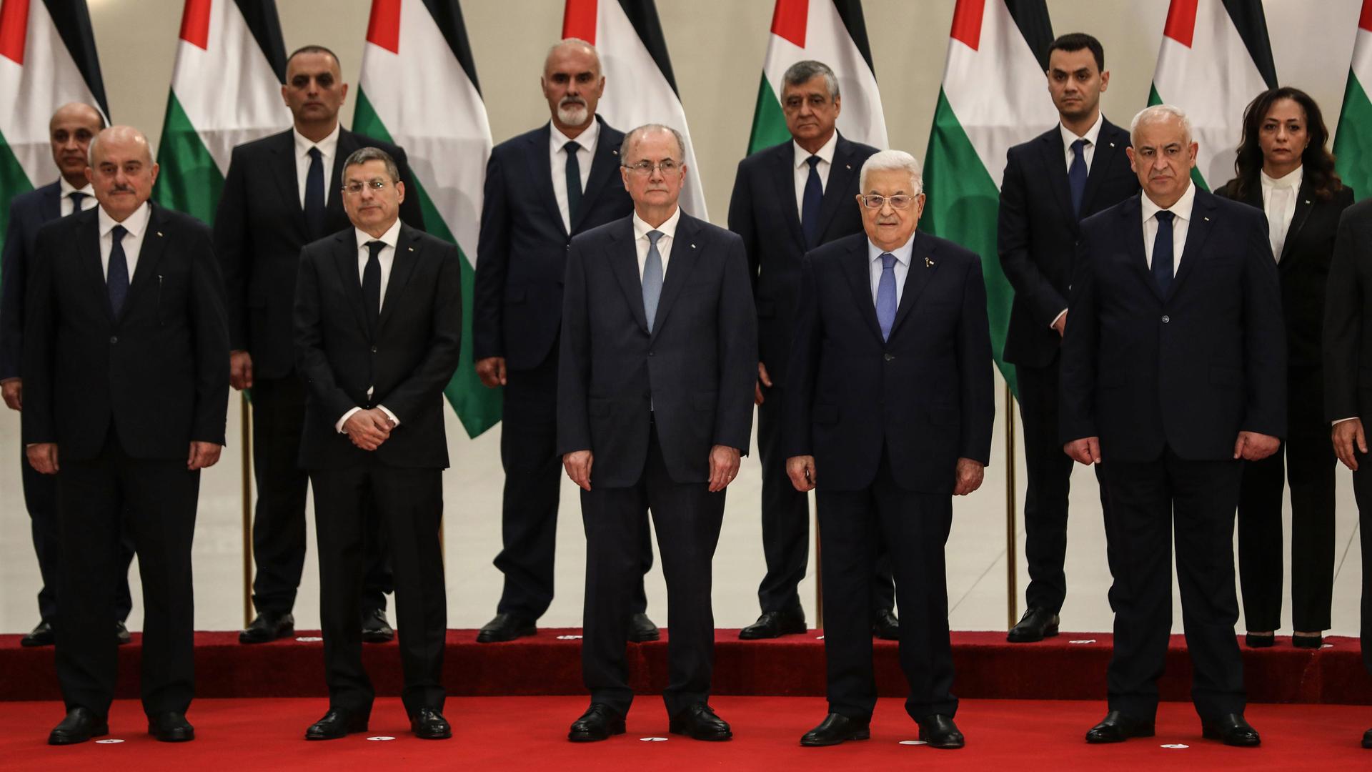 Der neue palästinensische Ministerpräsident Mustafa und Palästinenserpräsident Abbas mit einigen Mitgliedern des neuen Kabinetts. Sie stehen in zwei Reihen vor Palästina-Fahnen auf einem roten Teppich. Der neue palästinensische Ministerpräsident Mustafa und Palästinenserpräsident Abbas mit einigen Mitgliedern des neuen Kabinetts. Sie stehen in zwei Reihen vor Palästina-Fahnen auf einem roten Teppich.