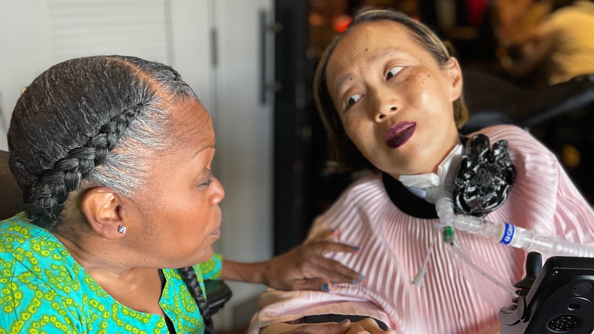Alice Wong (r.) sitzt in einem Roll-Stuhl. Sie schaut auf ihre Freundin Sandy Ho neben ihr. Alice Wong (r.) sitzt in einem Roll-Stuhl. Sie schaut auf ihre Freundin Sandy Ho neben ihr.