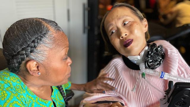 Alice Wong (r.) sitzt in einem Roll-Stuhl. Sie schaut auf ihre Freundin Sandy Ho neben ihr.