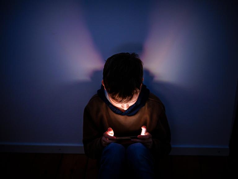 Symbolfoto. Gestellte Aufnahme zum Thema Kinder nutzen Social Media. Ein Junge sitzt in einem dunklen Raum und wird von einem Smartphone beleuchtet. Symbolfoto. Gestellte Aufnahme zum Thema Kinder nutzen Social Media. Ein Junge sitzt in einem dunklen Raum und wird von einem Smartphone beleuchtet.