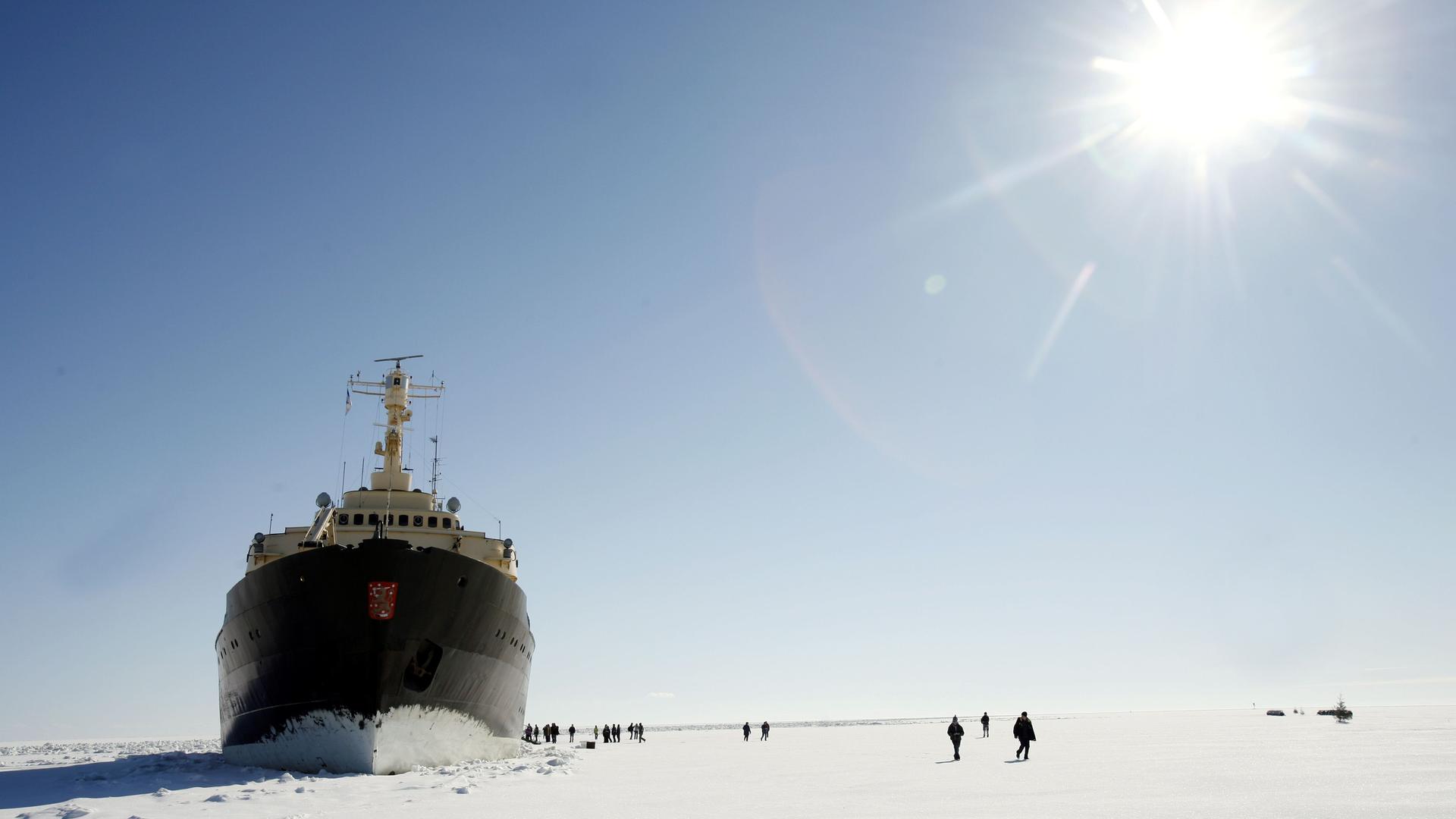 Der Passagier-Eisbrecher Sampo an der Nordspitze des Bottnischen Meerbusens im finnischen Lappland. Um das Schiff auf der Eisfläche sind relativ klein Menschen zu sehen.