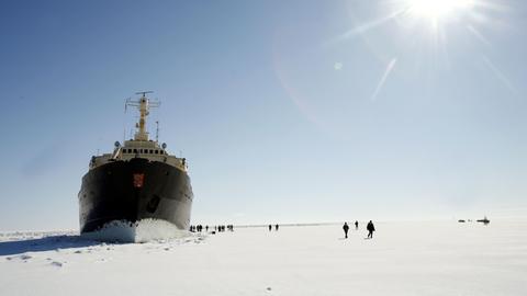 Der Passagier-Eisbrecher Sampo an der Nordspitze des Bottnischen Meerbusens im finnischen Lappland. Um das Schiff auf der Eisfläche sind relativ klein Menschen zu sehen.