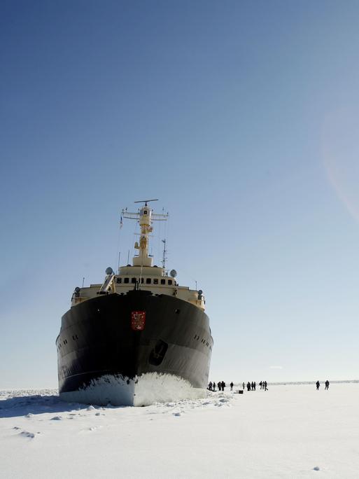 Der Passagier-Eisbrecher Sampo an der Nordspitze des Bottnischen Meerbusens im finnischen Lappland. Um das Schiff auf der Eisfläche sind relativ klein Menschen zu sehen.