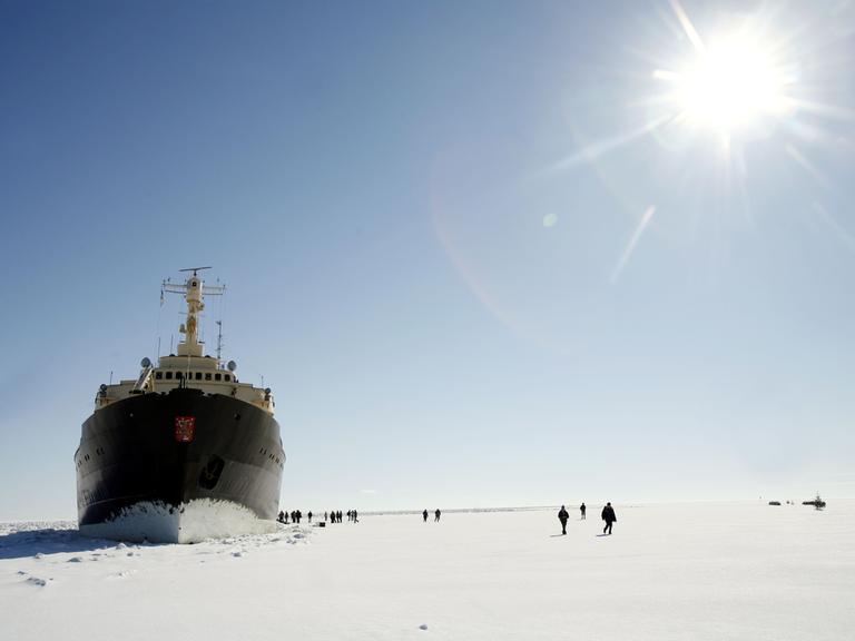 Der Passagier-Eisbrecher Sampo an der Nordspitze des Bottnischen Meerbusens im finnischen Lappland. Um das Schiff auf der Eisfläche sind relativ klein Menschen zu sehen.