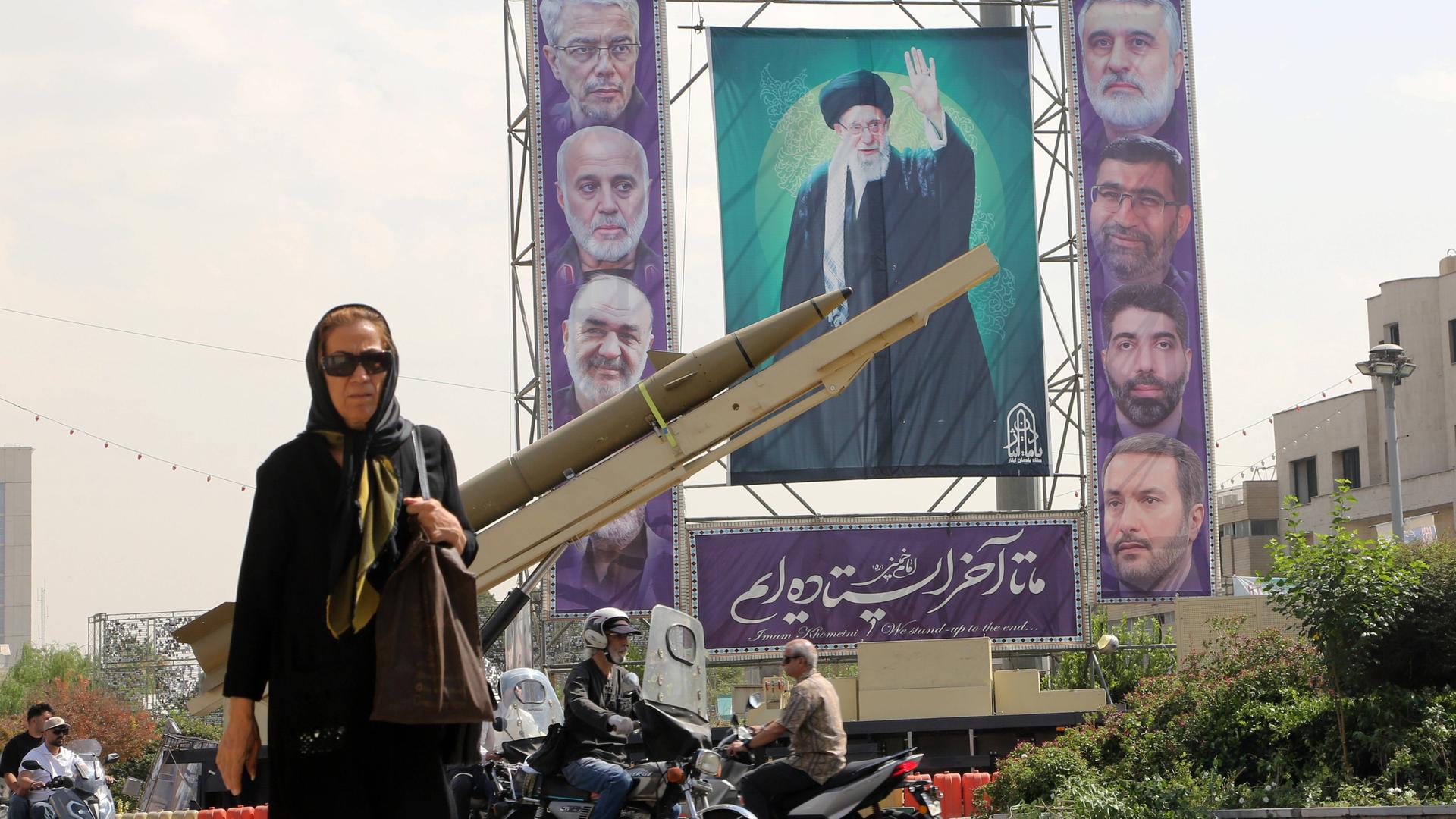 Eine Passantin auf dem Baharestan-Platz in Teheran, auf dem im Rahmen der iranischen Woche zum 45. Jahrestag des Iran-Irak-Krieges Miltitärgeräte und die Gesichter der iranishen Führung auf einem großen Plakat ausgestellt werden.
