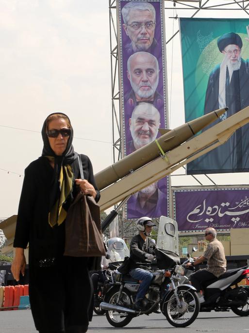 Eine Passantin auf dem Baharestan-Platz in Teheran, auf dem im Rahmen der iranischen Woche zum 45. Jahrestag des Iran-Irak-Krieges Miltitärgeräte und die Gesichter der iranishen Führung auf einem großen Plakat ausgestellt werden.