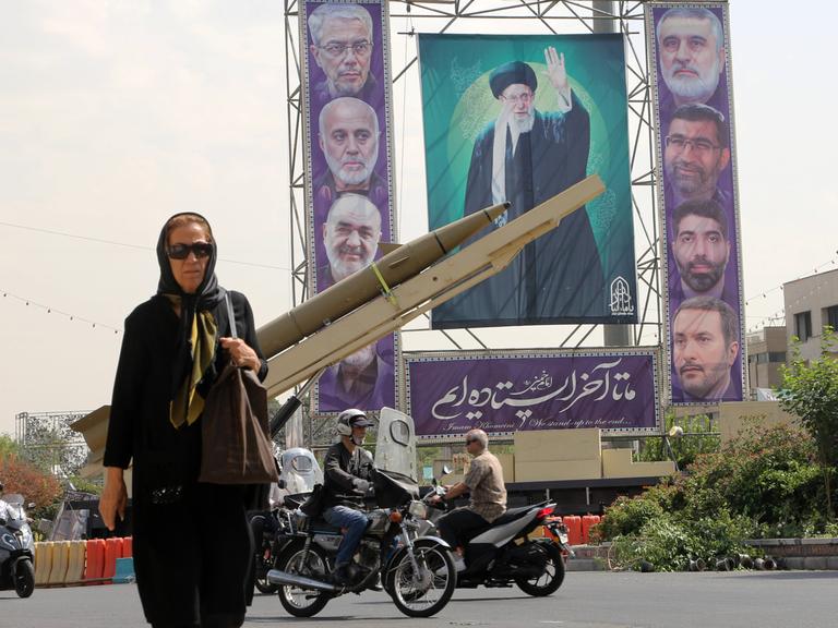 Eine Passantin auf dem Baharestan-Platz in Teheran, auf dem im Rahmen der iranischen Woche zum 45. Jahrestag des Iran-Irak-Krieges Miltitärgeräte und die Gesichter der iranishen Führung auf einem großen Plakat ausgestellt werden.