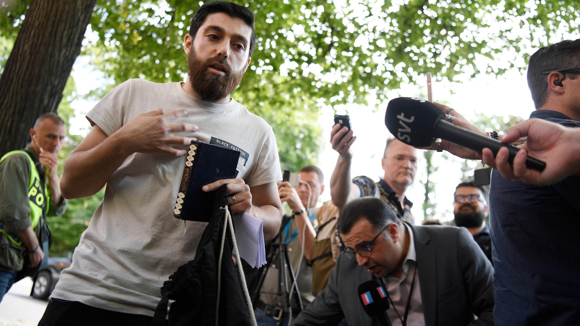 Ein Mann mit Büchern in Händen steht umringt von Journalisten und ihren Mikrofonen. Ein Mann mit Büchern in Händen steht umringt von Journalisten und ihren Mikrofonen.