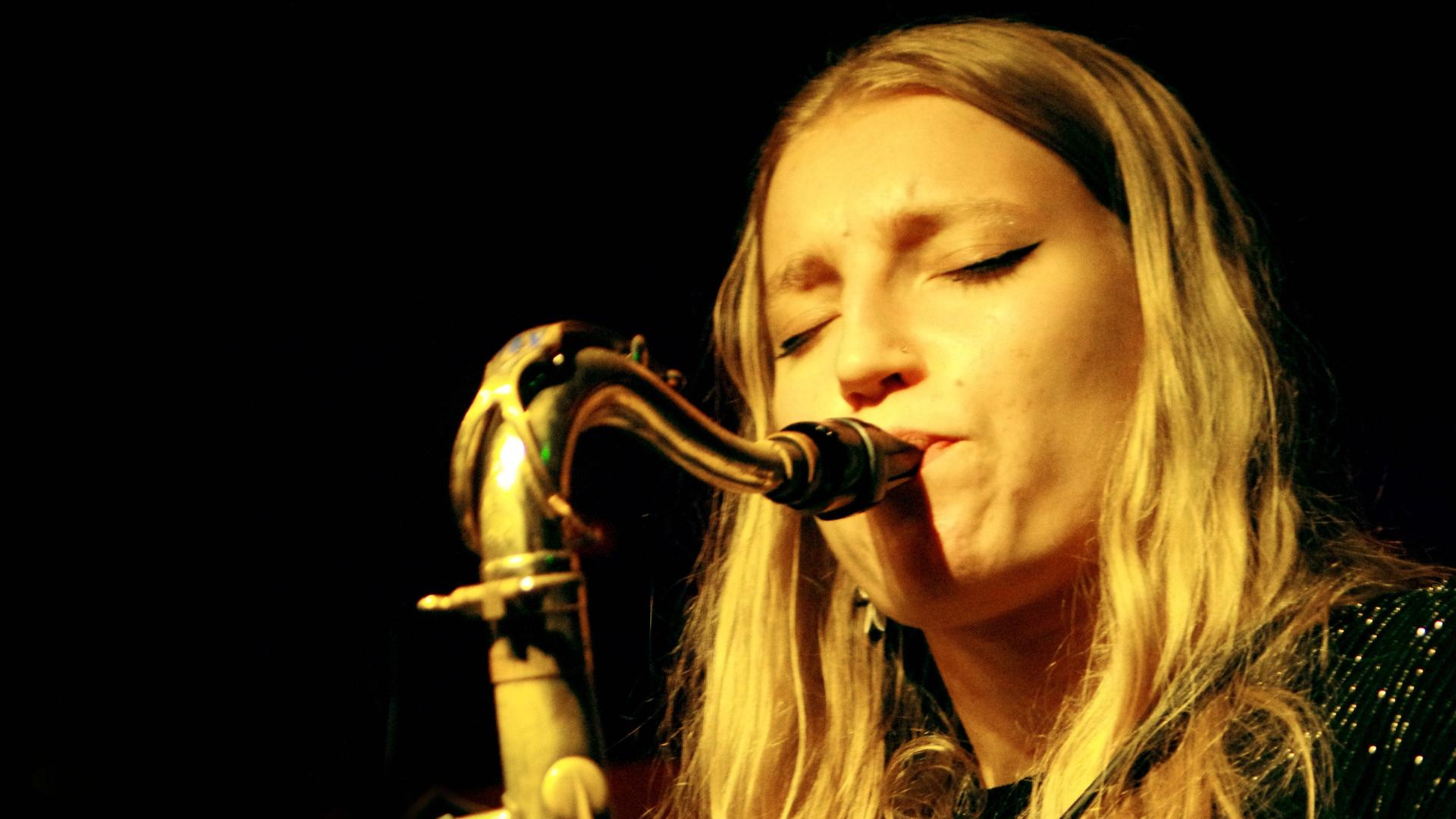 Blick auf das Gesicht der blonden, Saxofon spielenden Emma Rawicz.