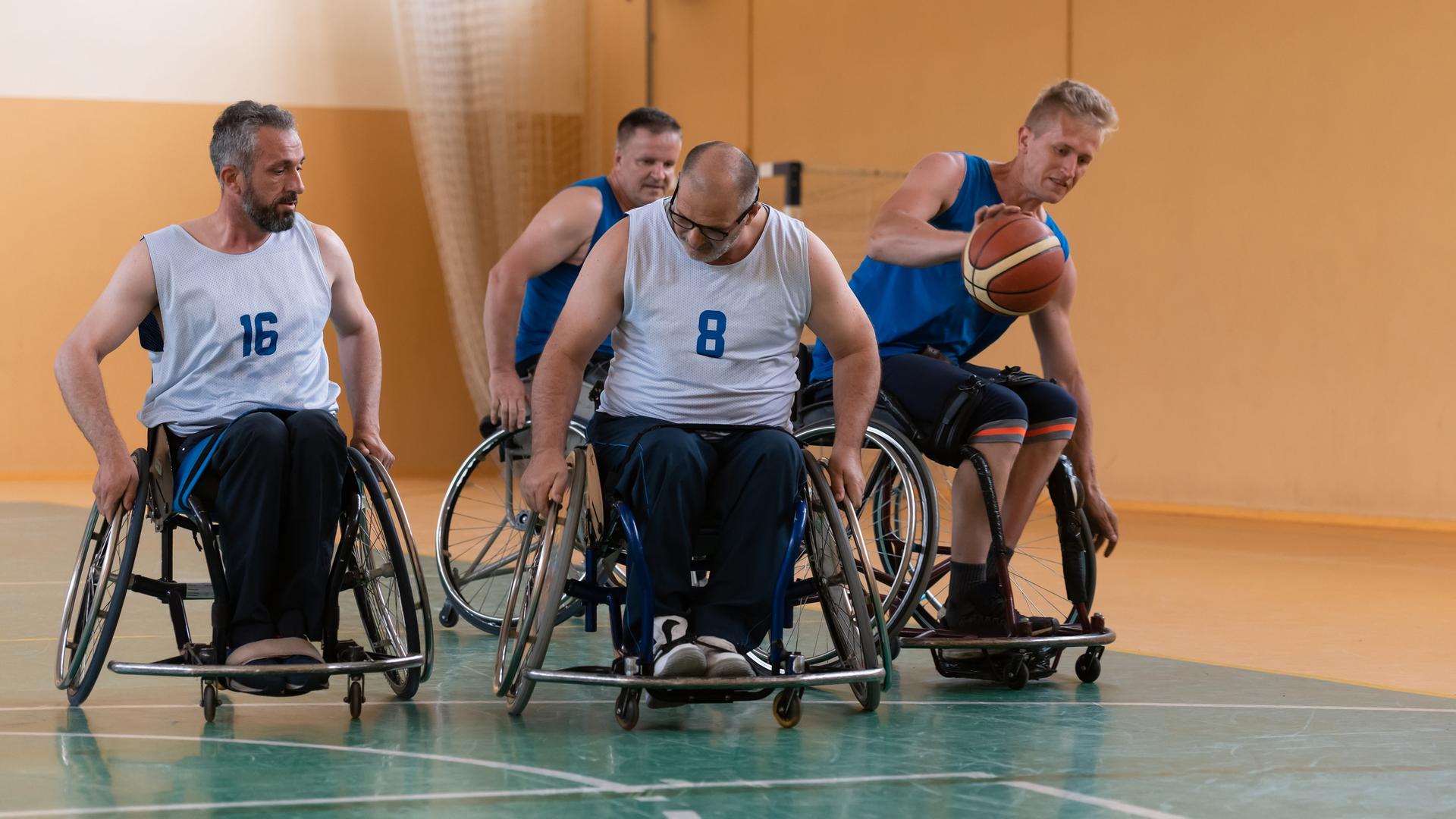 Vier Männer in Rollstühlen spielen Basketball in einer Halle. Vier Männer in Rollstühlen spielen Basketball in einer Halle.