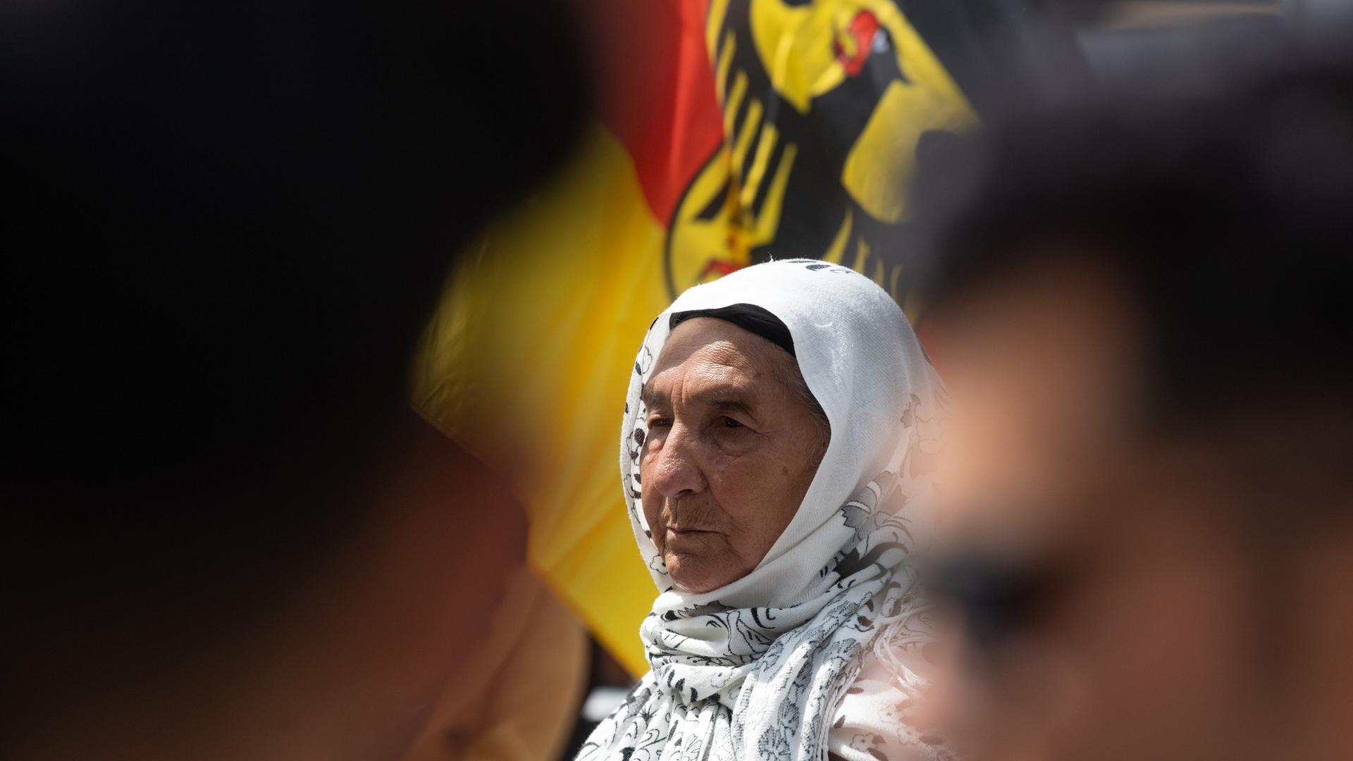 Eine Afghanin mit Kopfbedeckung ist zu sehen, hinter ihr ist eine Deutschlandfahne.
