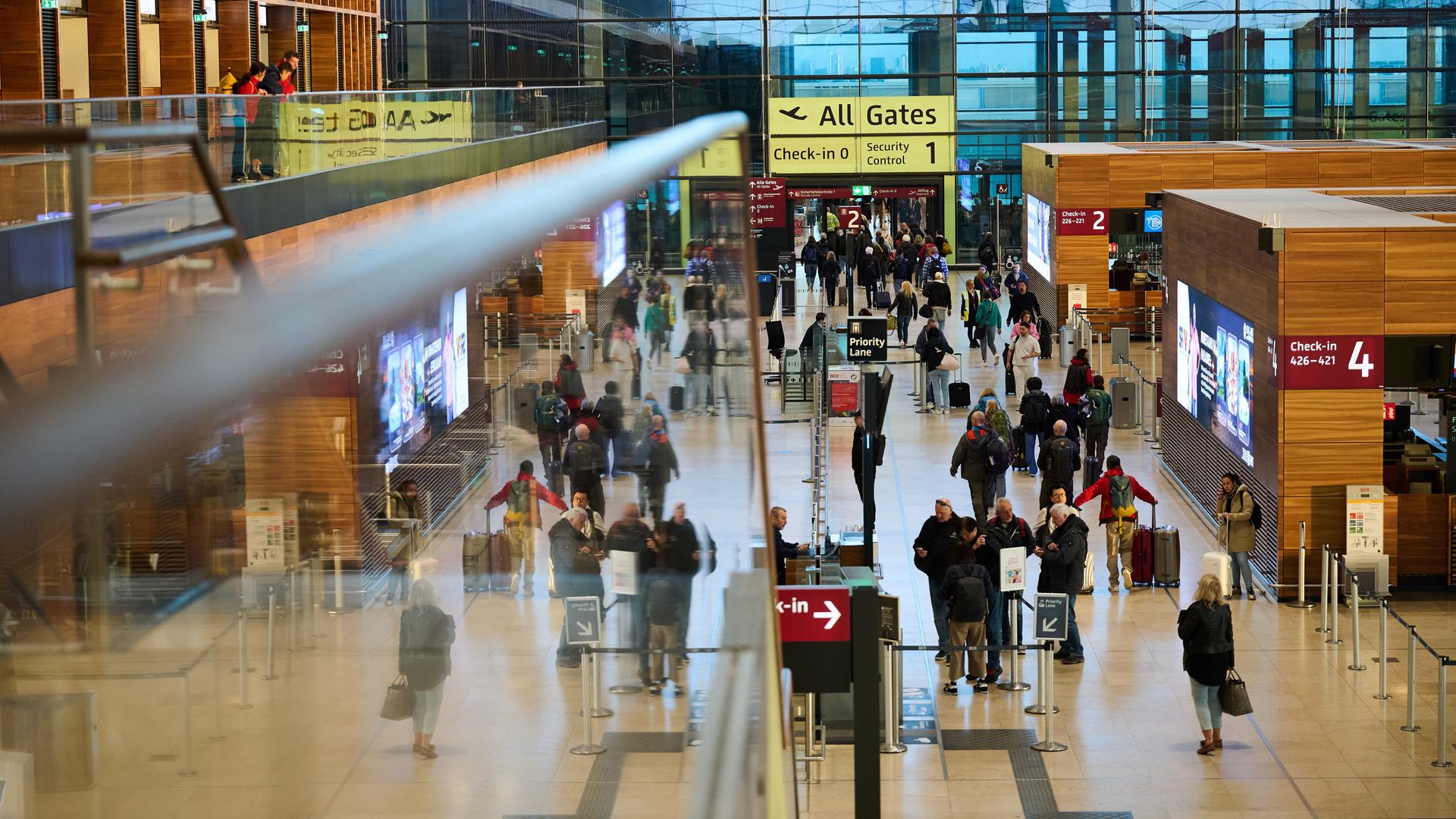 Blick in die Abfertigungshalle des Flughafens Berlin-Brandenburg: Anzeigetafeln, Hinweisschilder, Menschen mit Gepäck.