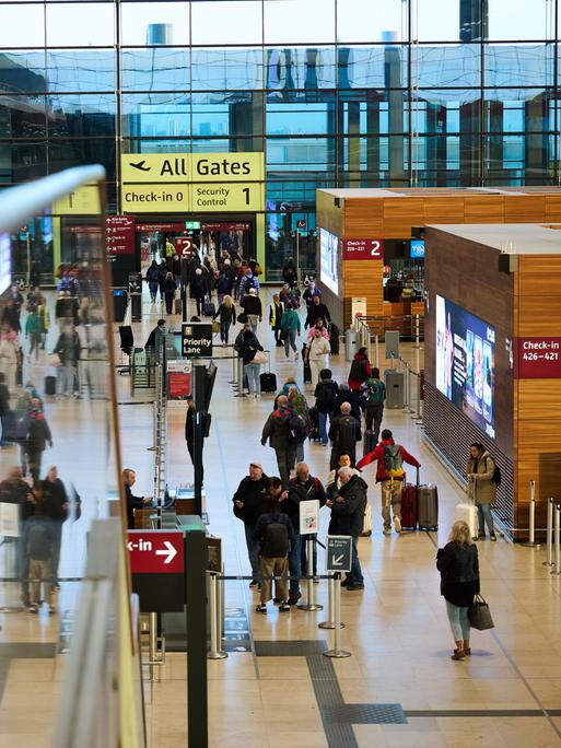 Blick in die Abfertigungshalle des Flughafens Berlin-Brandenburg: Anzeigetafeln, Hinweisschilder, Menschen mit Gepäck.