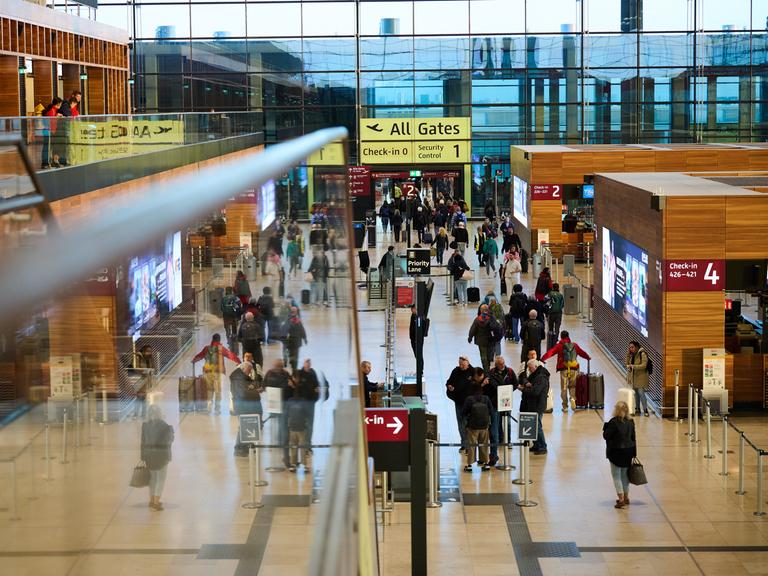 Blick in die Abfertigungshalle des Flughafens Berlin-Brandenburg: Anzeigetafeln, Hinweisschilder, Menschen mit Gepäck.