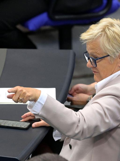 Renate Künast sitzt im Bundestag und zeigt mit ihrem Finger in Richtung des Rednerpults, vor ihr liegt ein Handy