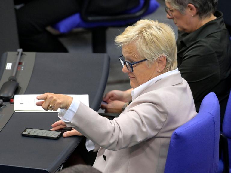 Renate Künast sitzt im Bundestag und zeigt mit ihrem Finger in Richtung des Rednerpults, vor ihr liegt ein Handy