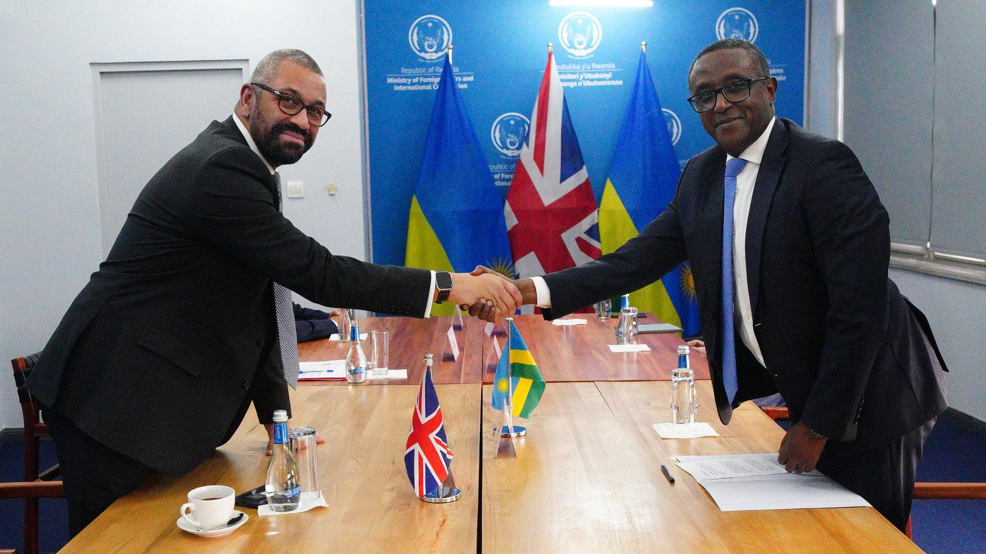 Kigali: James Cleverly (l), Innenminister von Großbritannien, und Vincent Birut, Außenminister von Ruanda, halten ein bilaterales Treffen ab, nachdem sie einen neuen Vertrag unterzeichnet haben. Sie schütteln sich über den Tisch hinweg die Hände.