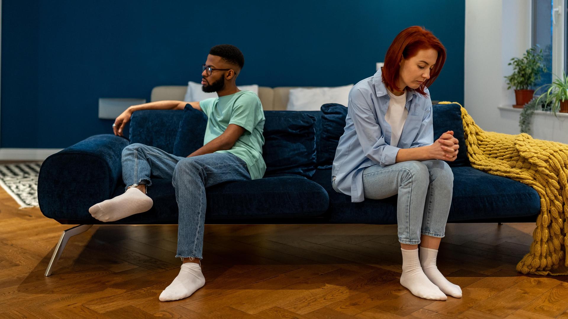 Ein Paar sitzt getrennt auf einem Sofa und sieht unglücklich aus, sie reden nicht miteinander Ein Paar sitzt getrennt auf einem Sofa und sieht unglücklich aus, sie reden nicht miteinander