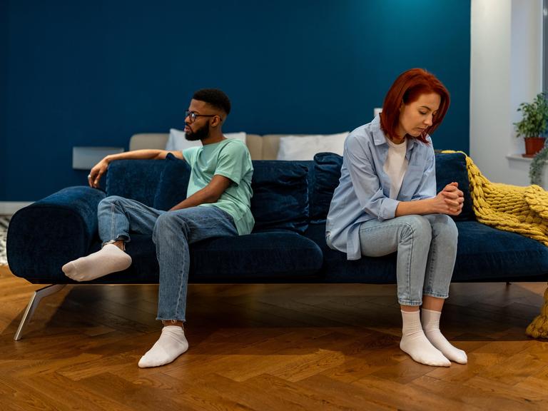 Ein Paar sitzt getrennt auf einem Sofa und sieht unglücklich aus, sie reden nicht miteinander