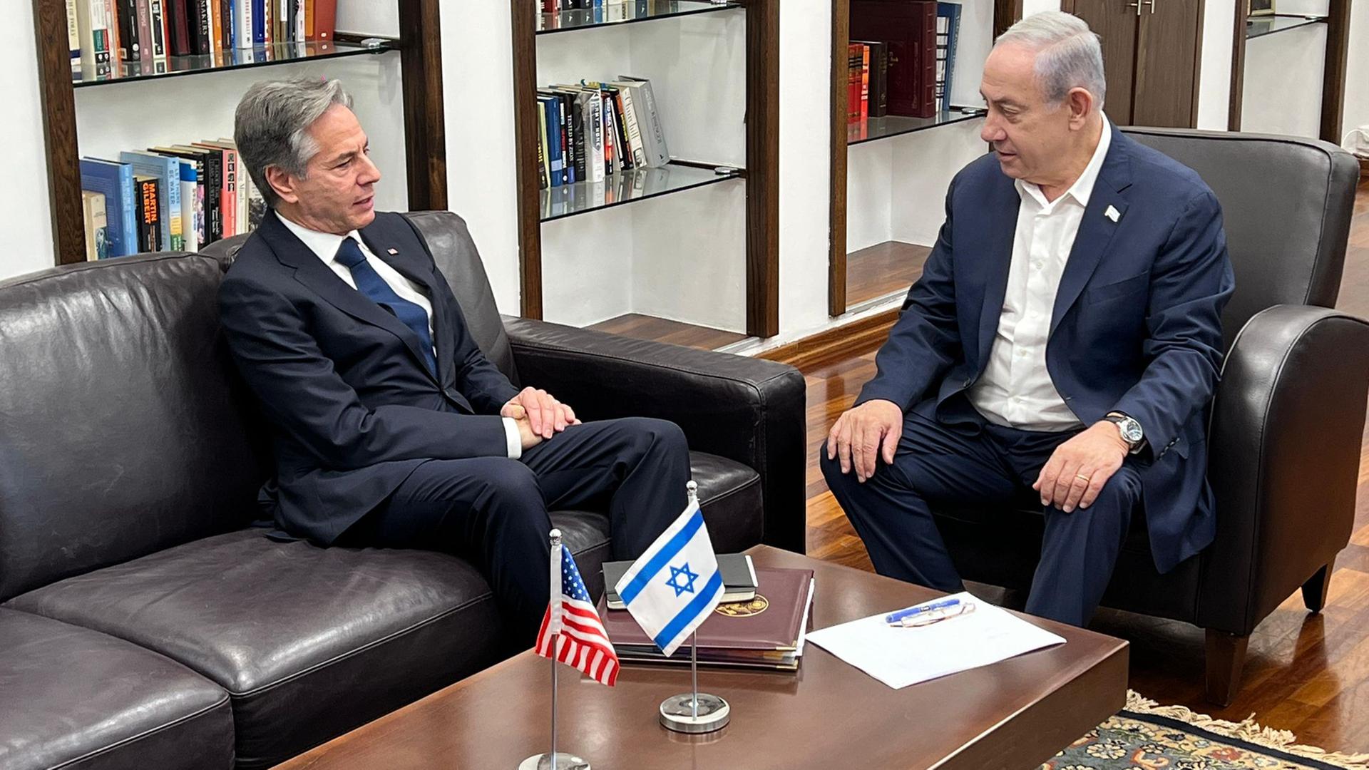 Das Foto zeigt US-Außenminister Blinken und den israelischen Ministerpräsidenten Netanjahu. Die Politiker sitzen an einem Tisch, auf dem die Flaggen Israels und der USA aufgestellt wurden.