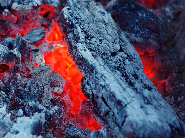 Zu sehen: Nahaufnahme eines Feuerst mit Glut und Asche. 