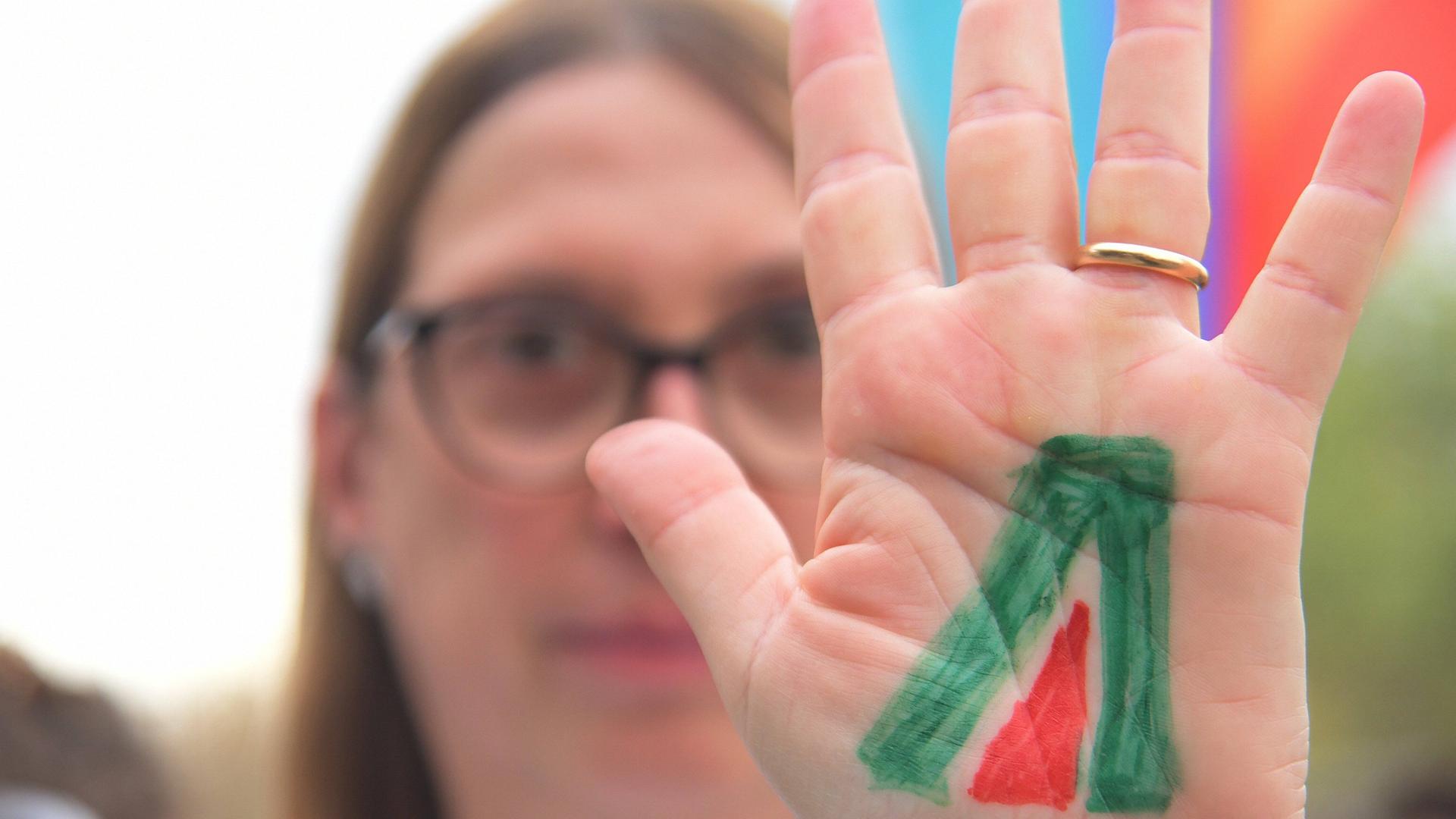 Eine Frau mit Brille streckt ihre Handfläche nach vorne. Auf der Handfläche ist ein grün-rotes Symbol.