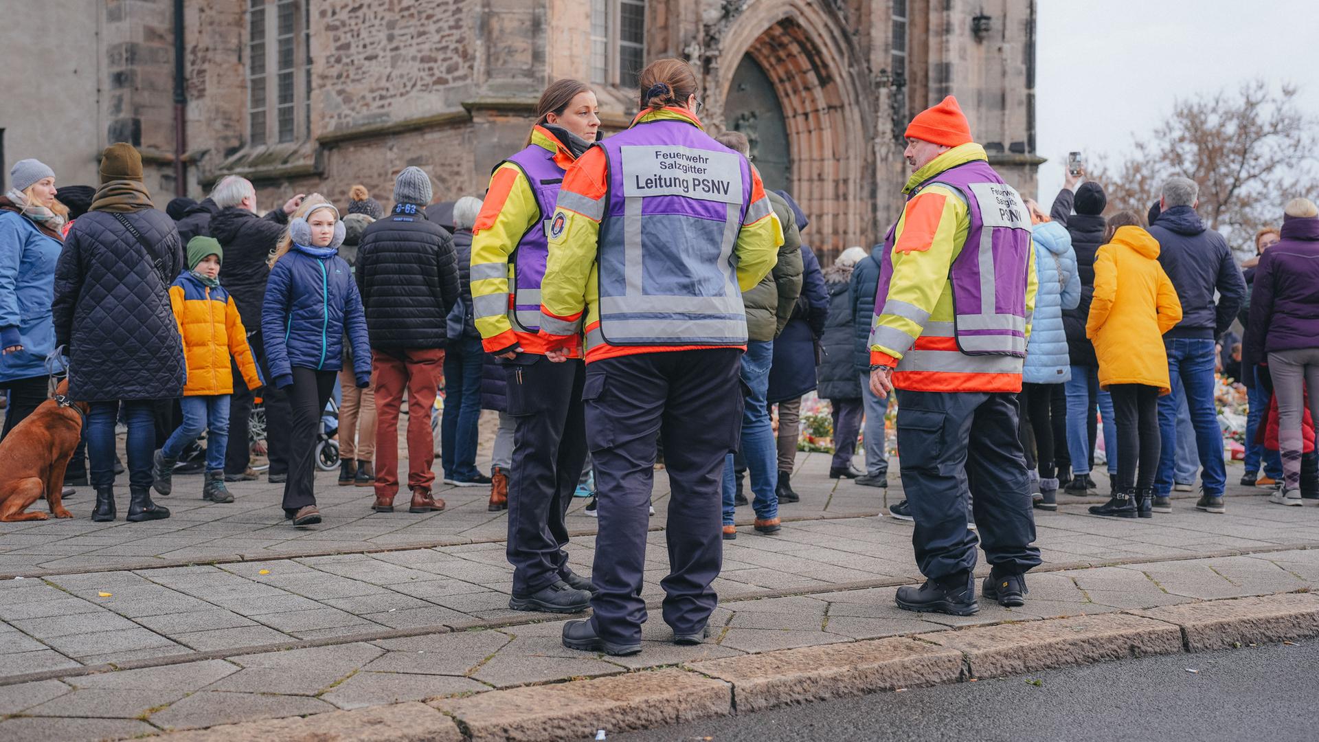 Einsatzkräfte in orangefarbenen Jacken und andere Menschen stehen vor der Trauerstelle am Dom nach dem Anschlag auf den Magdeburger Weihnachtsmarkt