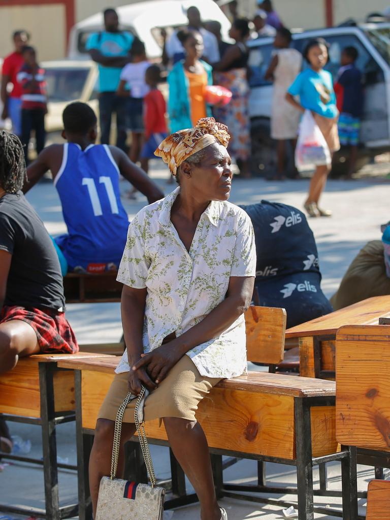 Mehrere Menschen sitzen vor einer Schule, die im Bezirk der Brothers Road in Petion-Ville als Unterkunft dient, auf Möbeln und warten. 